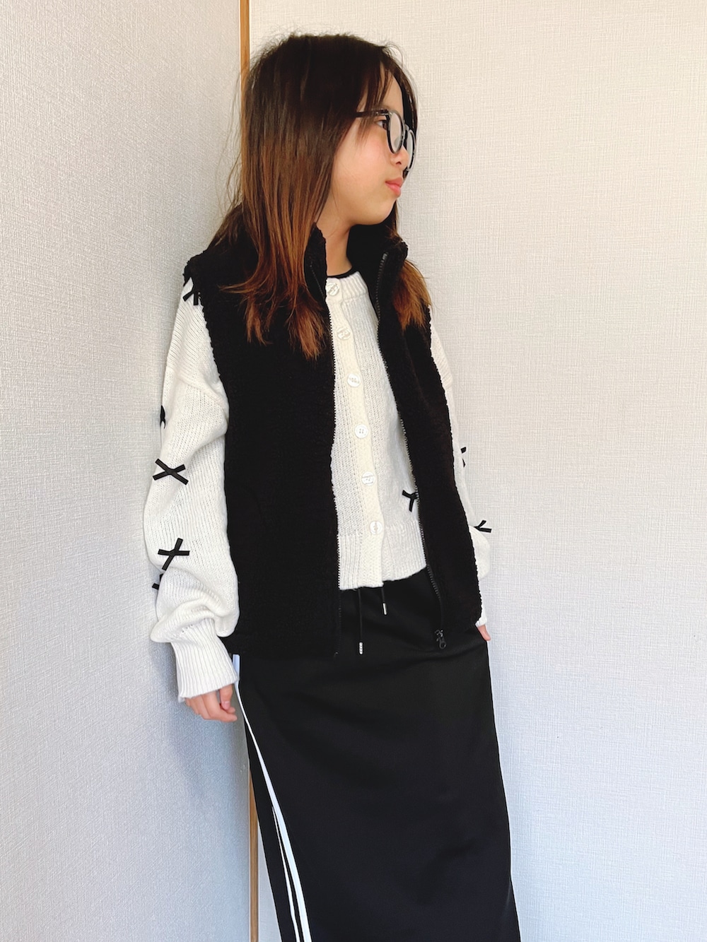 ホワイト系のニット/セーター、ブラック系のスカート、ブラック系のベストを着用したキッズの冬コーディネートの2枚目の写真