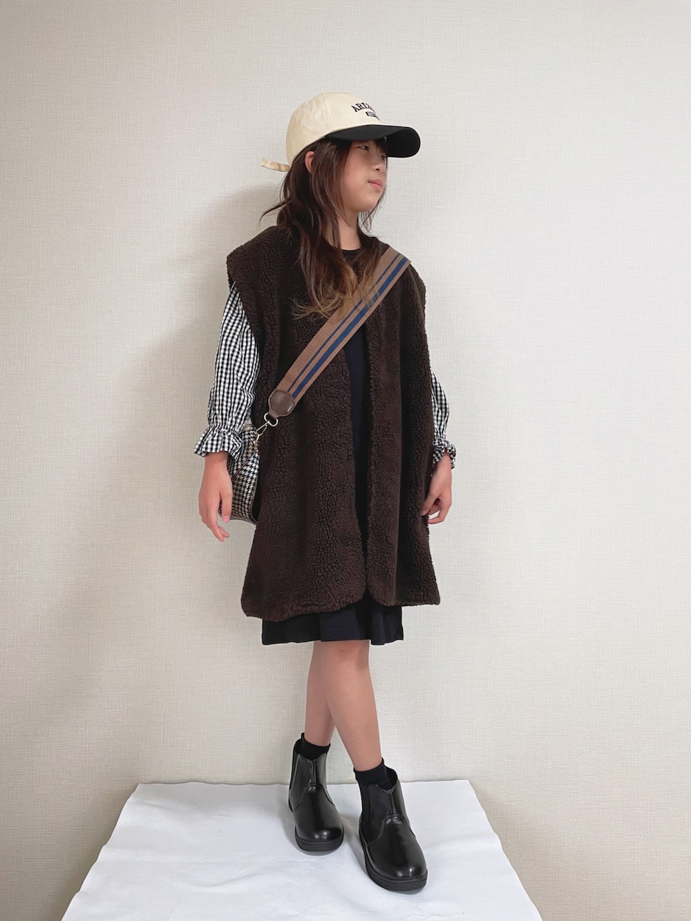 ブラック系のワンピース、ブラウン系のショルダーバッグ、ブラック系のブーツを着用したキッズの秋コーディネートの2枚目の写真