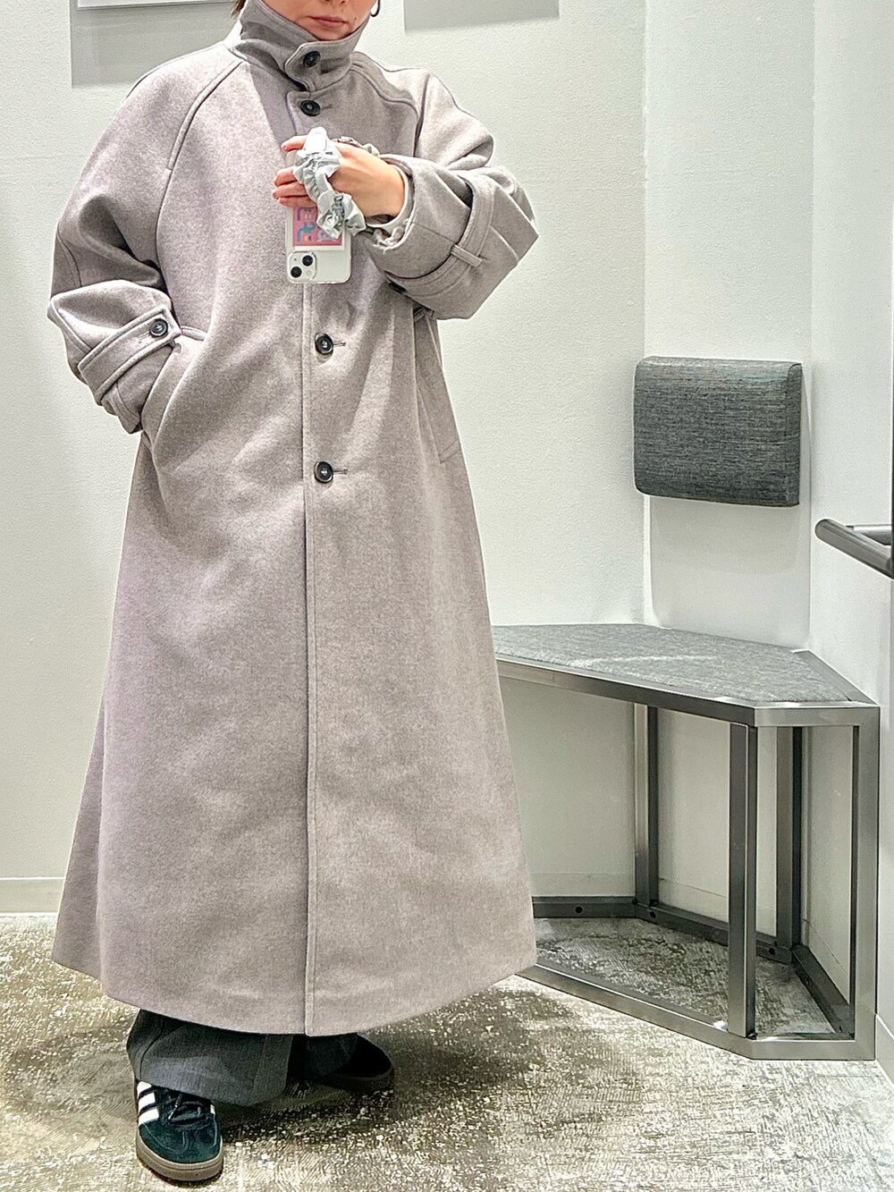 グレー系のステンカラーコート、ブラック系のスニーカーを着用したレディースの秋コーディネートの2枚目の写真