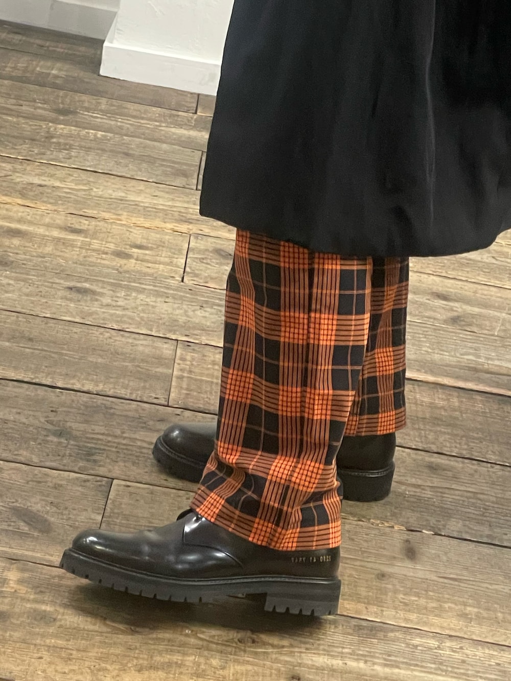 ブラック系のステンカラーコート、ブラック系のブーツ、オレンジ系のその他パンツを着用したメンズの冬コーディネートの3枚目の写真