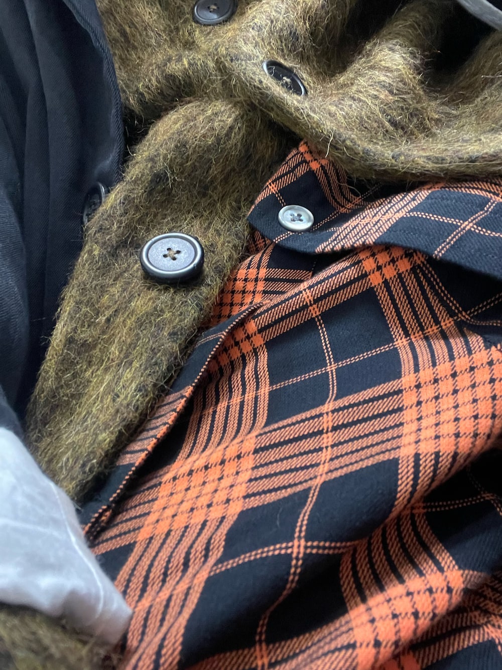 ブラック系のステンカラーコート、ブラック系のブーツ、オレンジ系のその他パンツを着用したメンズの冬コーディネートの2枚目の写真