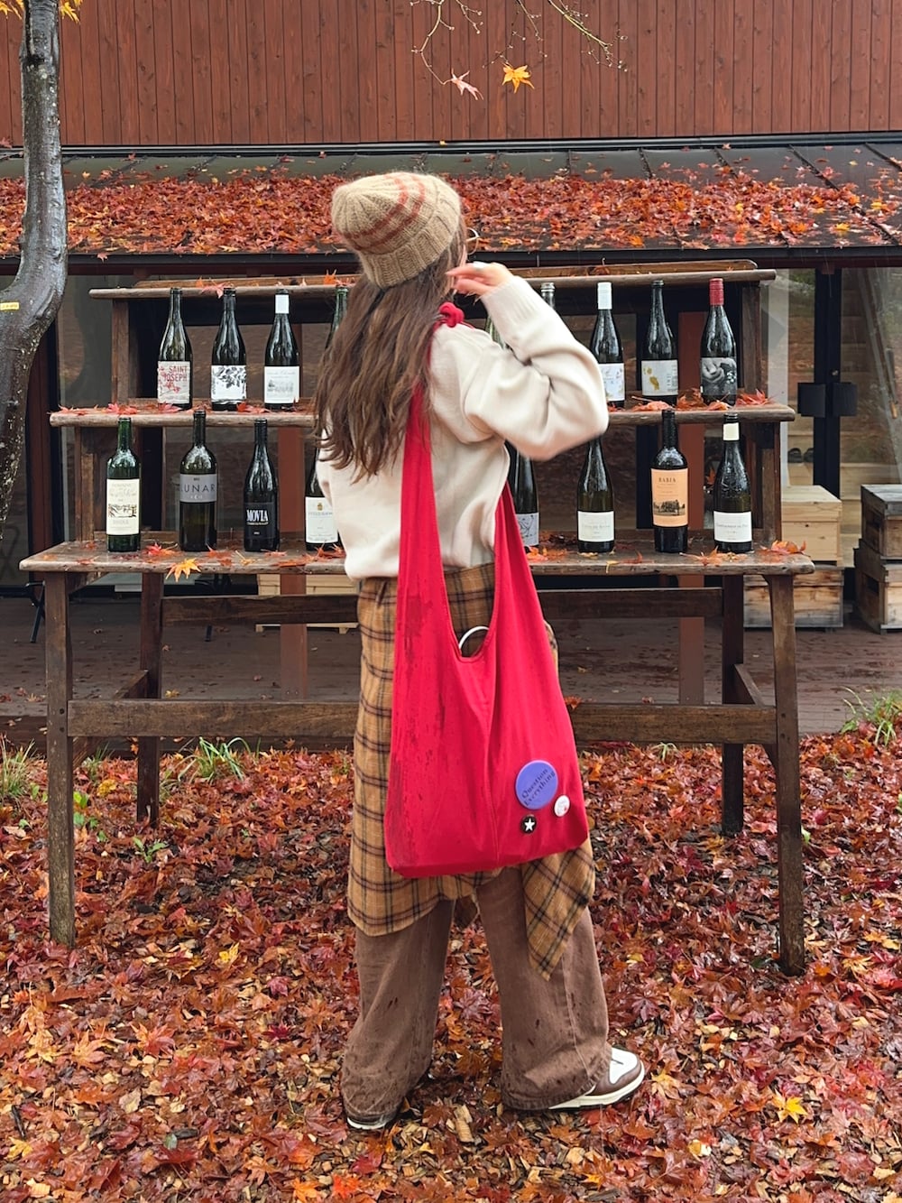 ブラウン系のデニムパンツ、レッド系のショルダーバッグ、ホワイト系のスニーカーを着用したレディースの秋コーディネートの2枚目の写真