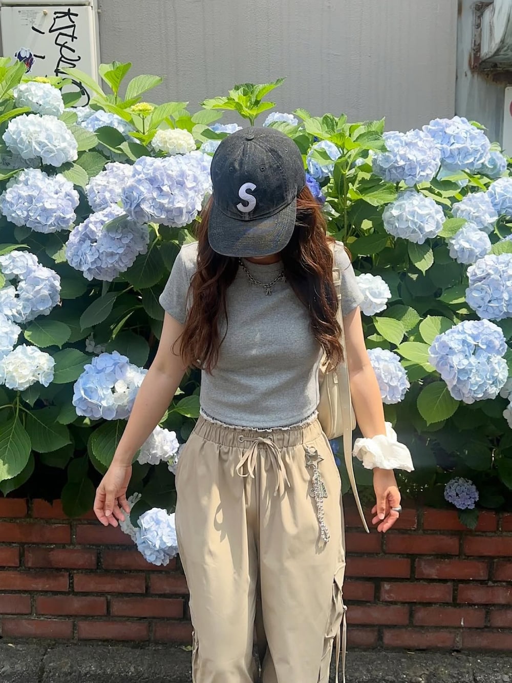 ベージュ系のハンドバッグ、グレー系のTシャツ/カットソー、ホワイト系のスニーカーを着用したレディースの夏コーディネートの2枚目の写真