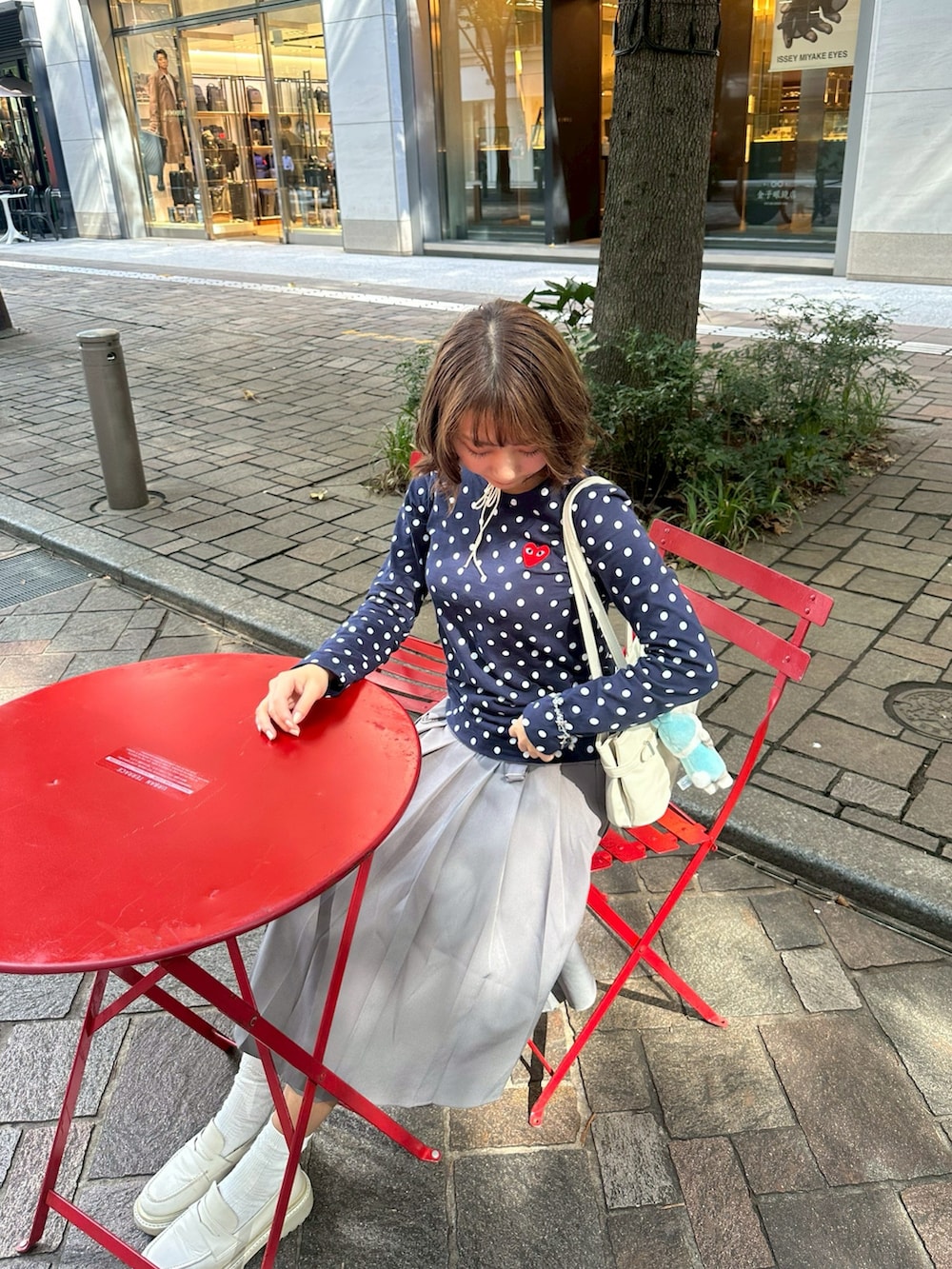 グレー系のスカート、ブルー系のTシャツ/カットソー、ホワイト系のショルダーバッグを着用したレディースの秋コーディネートの2枚目の写真