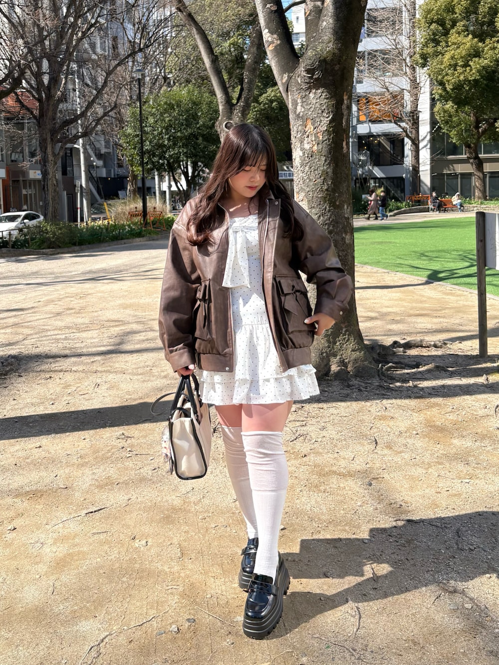 ブラウン系のライダースジャケット、ブラック系のワンピース、ホワイト系のトートバッグを着用したレディースの春コーディネートの2枚目の写真