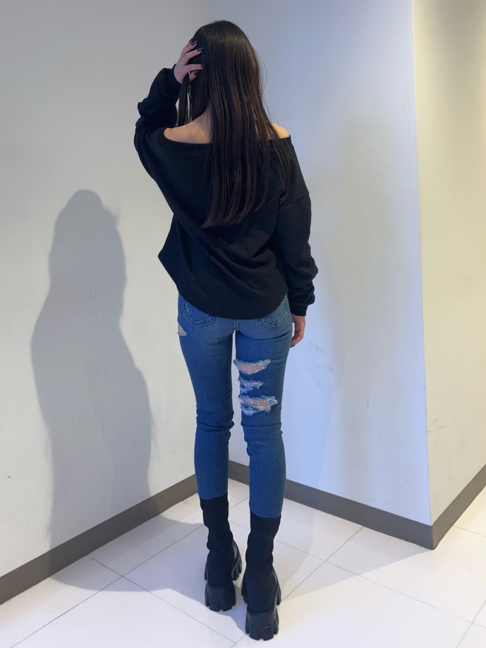 ブラック系のスウェット、ブルー系のデニムパンツ、ブラック系のブーツを着用したレディースの秋コーディネートの3枚目の写真