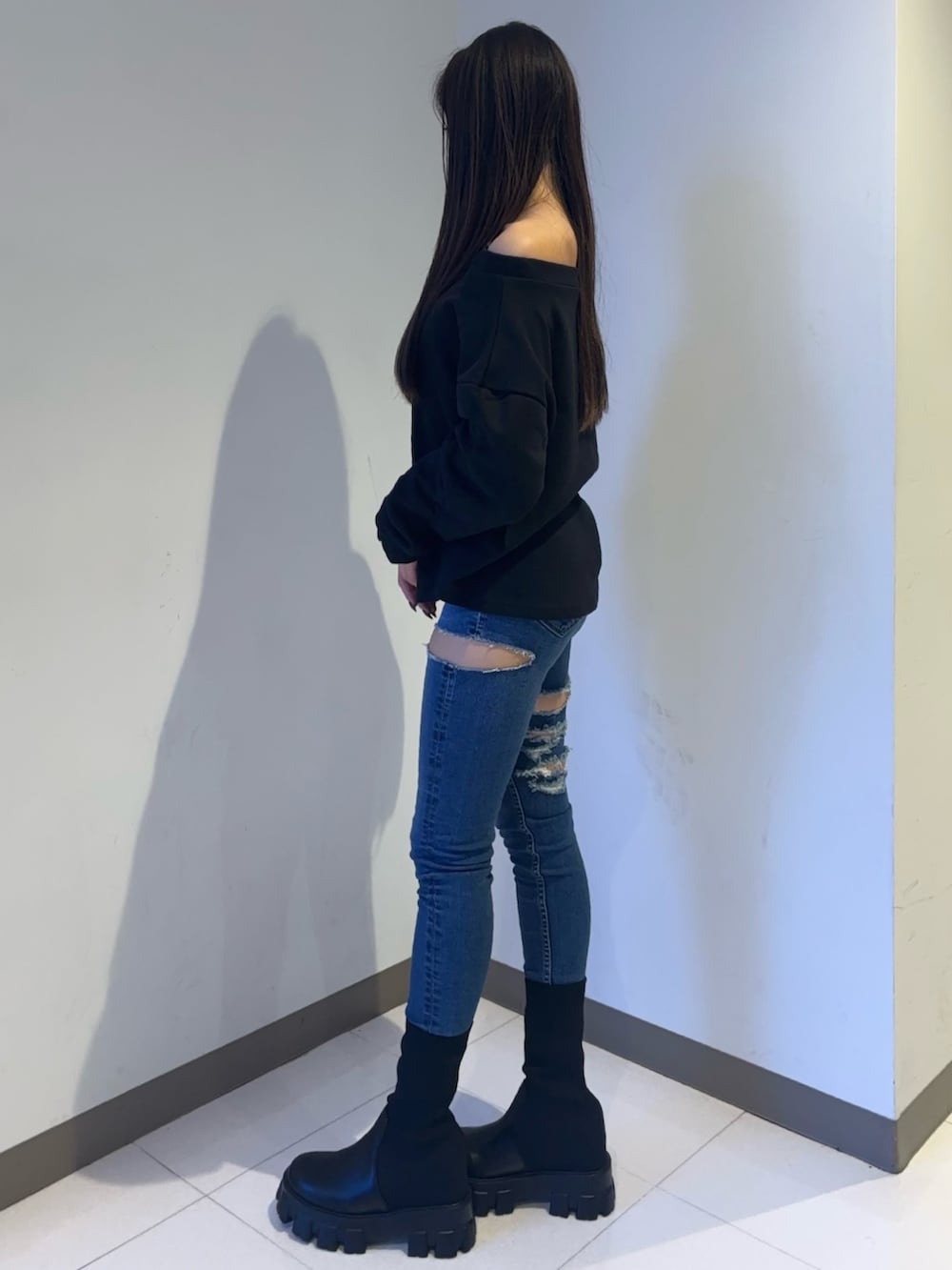 ブラック系のスウェット、ブルー系のデニムパンツ、ブラック系のブーツを着用したレディースの秋コーディネートの2枚目の写真