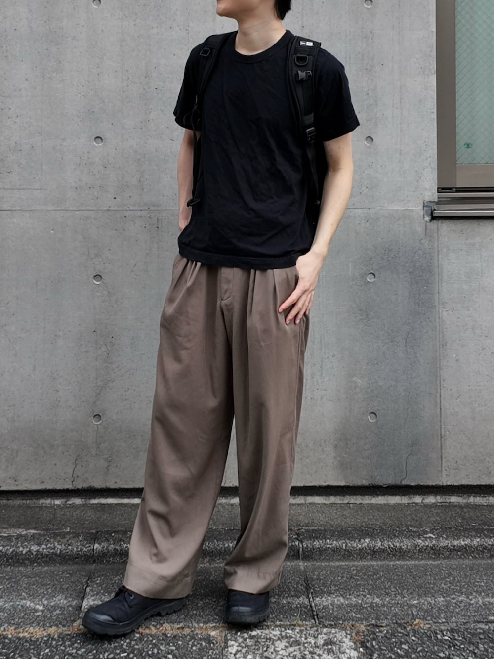 グレー系のスラックス、ブラック系のバックパック/リュック、ブラック系のトップスを着用したメンズの夏コーディネートの2枚目の写真