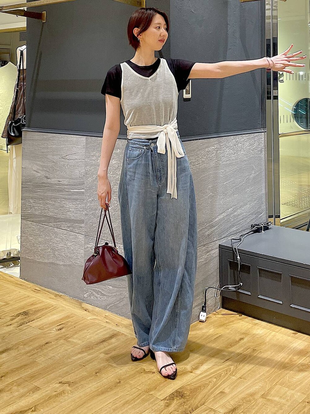 レッド系のショルダーバッグ、ブルー系のデニムパンツ、ブラック系のサンダルを着用したレディースの夏コーディネートの2枚目の写真