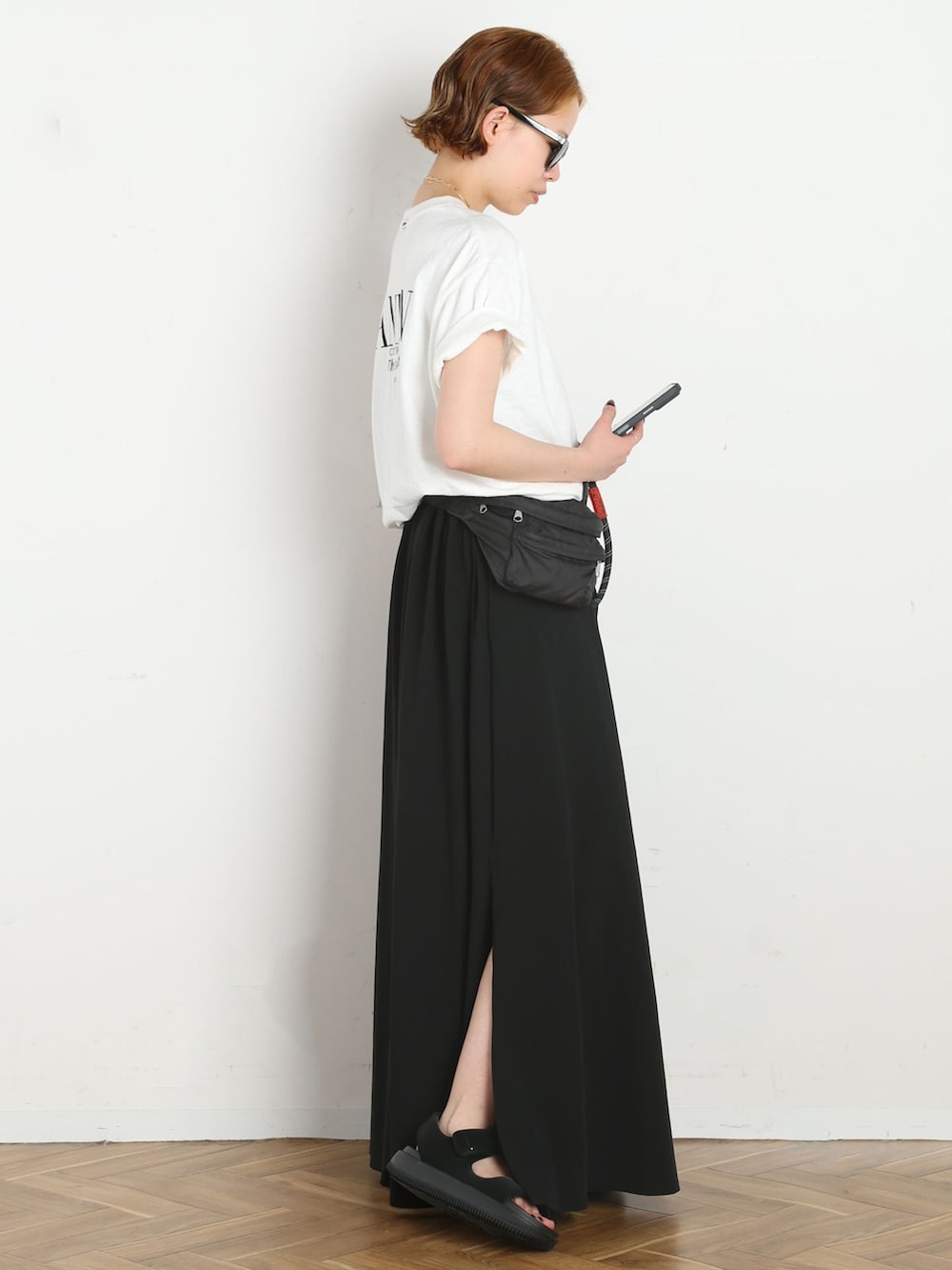 ブラック系のスカート、ホワイト系のTシャツ/カットソー、ブラック系のサンダルを着用したレディースの春コーディネートの2枚目の写真