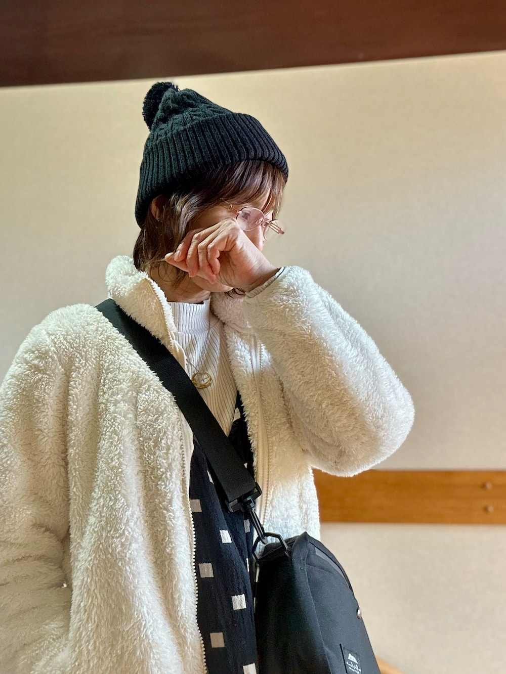 ホワイト系のその他アウター、ベージュ系のTシャツ/カットソー、ブラック系のジャンパースカートを着用したレディースの冬コーディネートの2枚目の写真