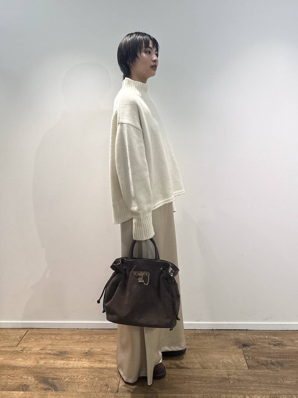 ホワイト系のニット/セーター、ブラウン系のブーツ、ブラウン系のトートバッグを着用したレディースの秋コーディネートの2枚目の写真