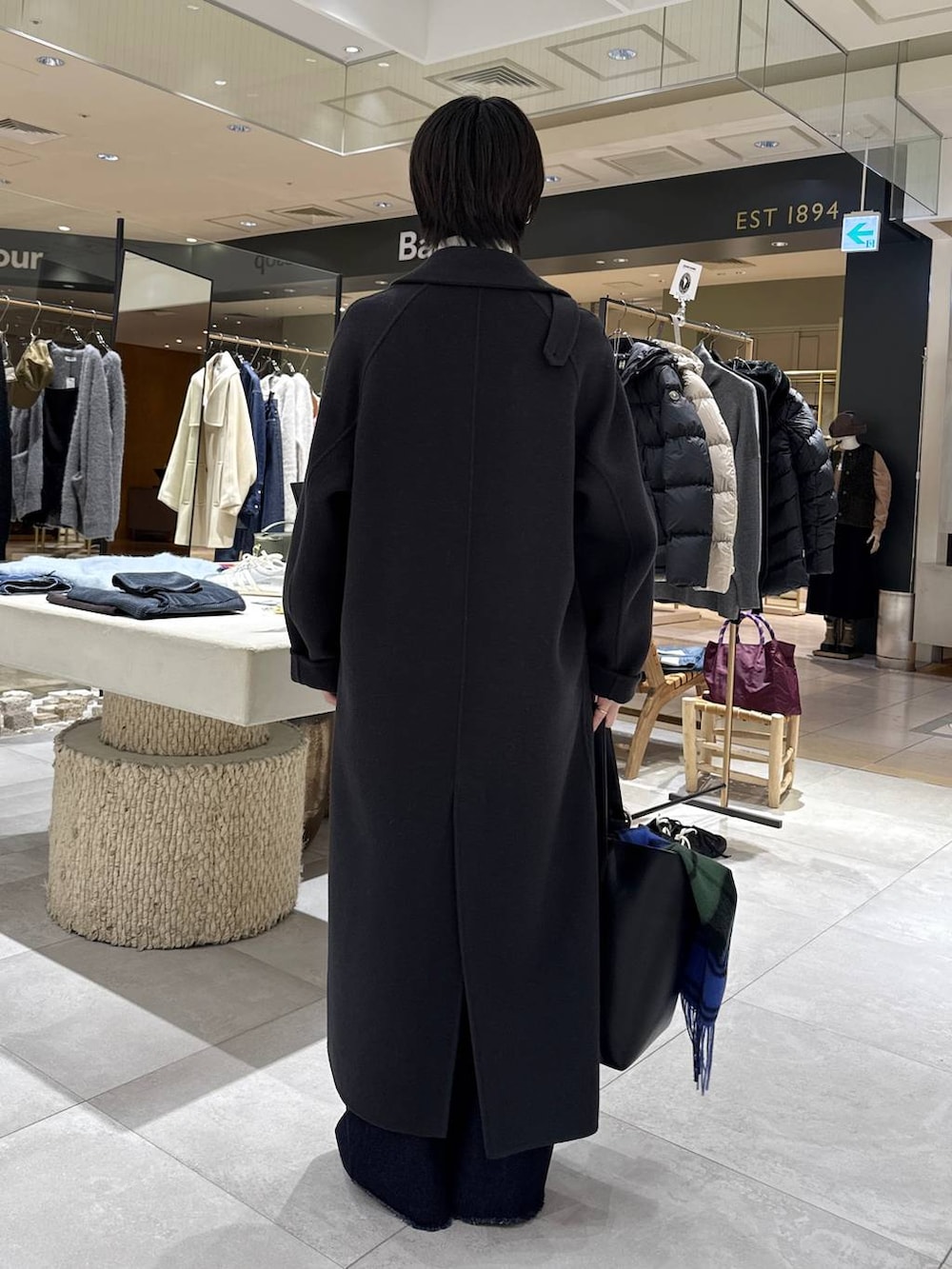 グレー系のステンカラーコート、ホワイト系のニット/セーター、ブラック系のハンドバッグを着用したレディースの秋コーディネートの3枚目の写真