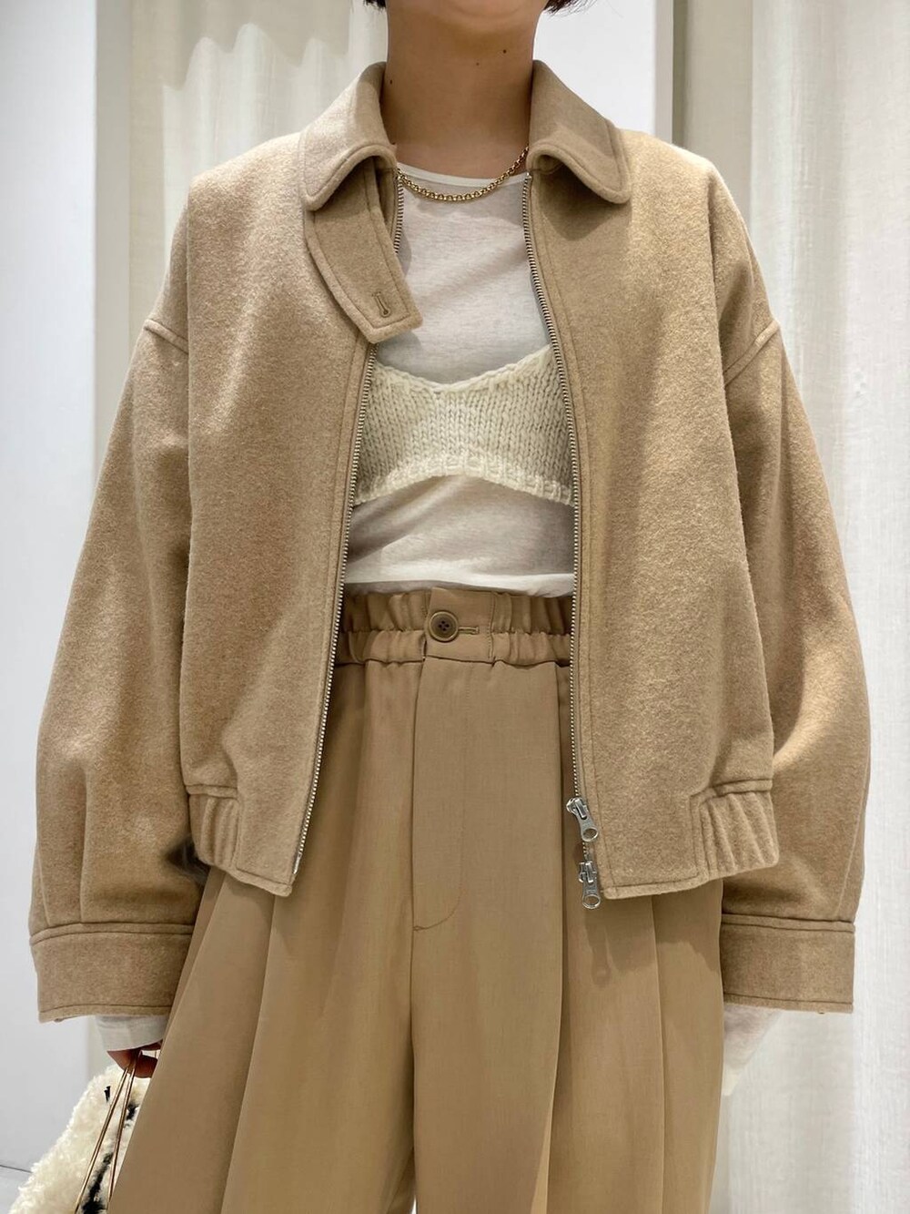 ホワイト系のハンドバッグ、ホワイト系のニット/セーター、ベージュ系のブルゾンを着用したレディースの秋コーディネートの4枚目の写真