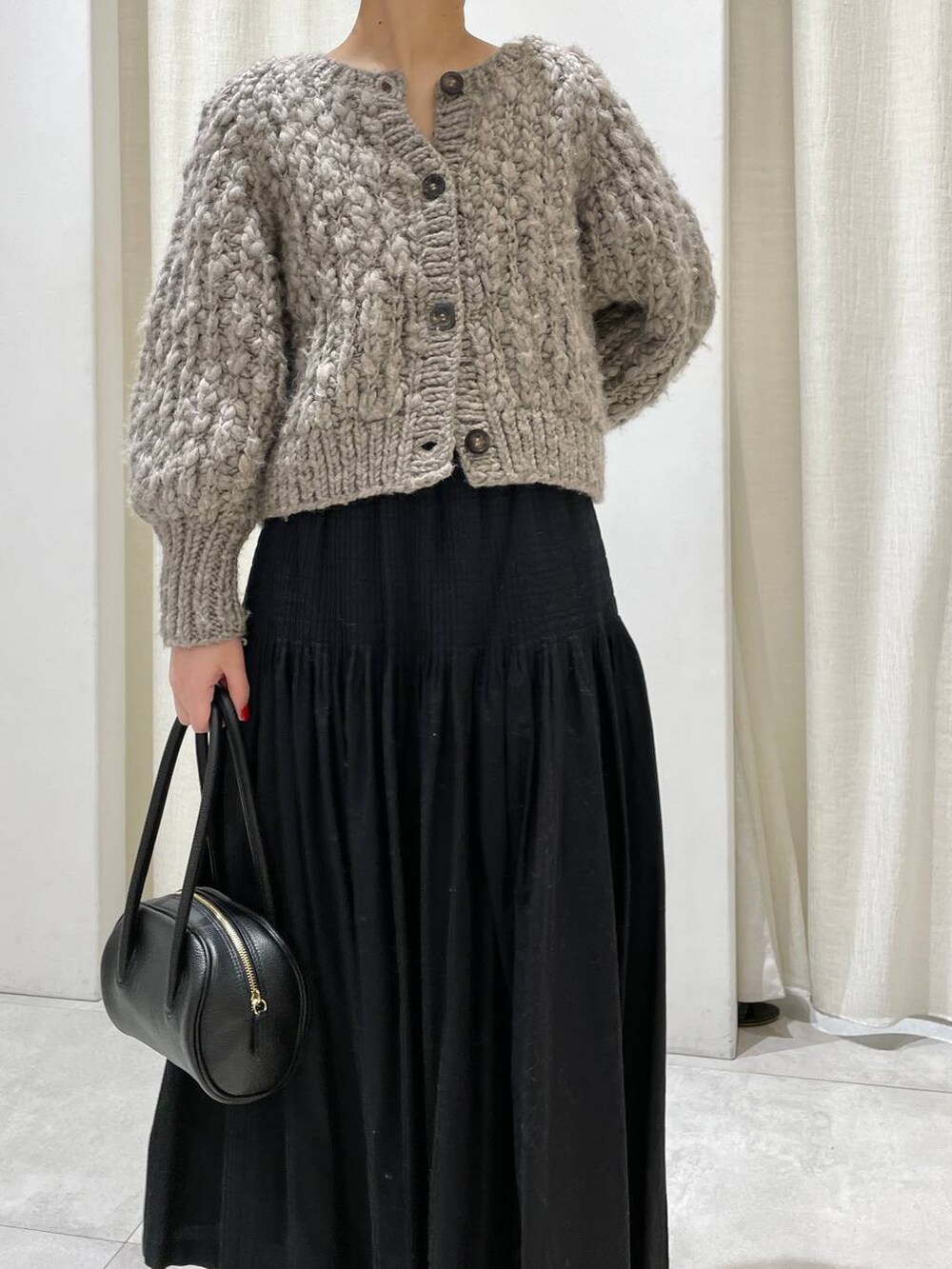 ベージュ系のカーディガン/ボレロ、ブラック系のスカートを着用したレディースの冬コーディネートの2枚目の写真