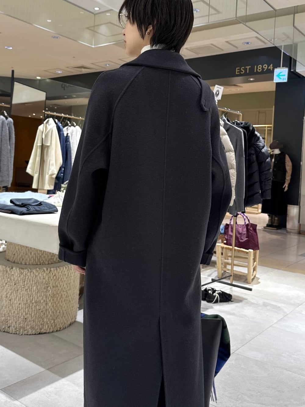 グレー系のステンカラーコート、ホワイト系のニット/セーター、ブラック系のハンドバッグを着用したレディースの秋コーディネートの4枚目の写真