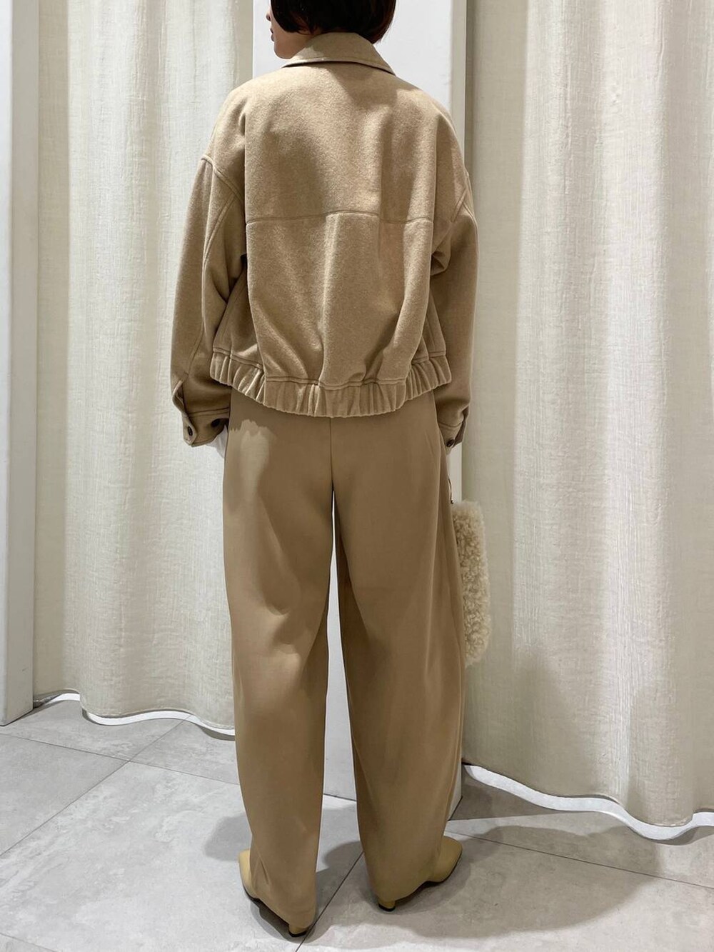 ホワイト系のハンドバッグ、ホワイト系のニット/セーター、ベージュ系のブルゾンを着用したレディースの秋コーディネートの3枚目の写真