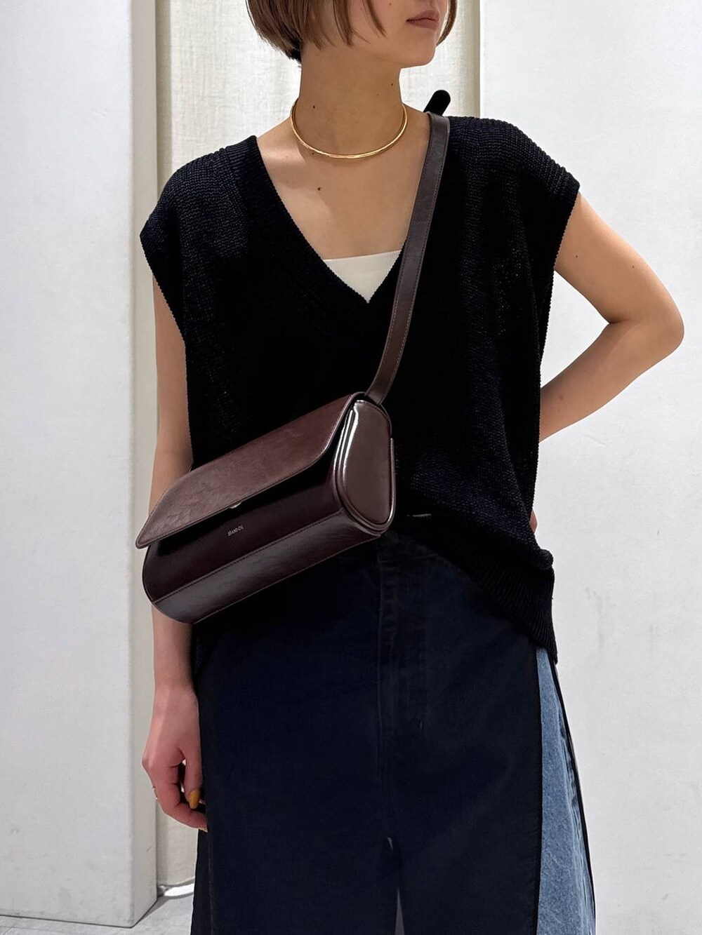 ブラック系のスカート、ブルー系のデニムパンツ、ブラウン系のパンプスを着用したレディースの春コーディネートの2枚目の写真