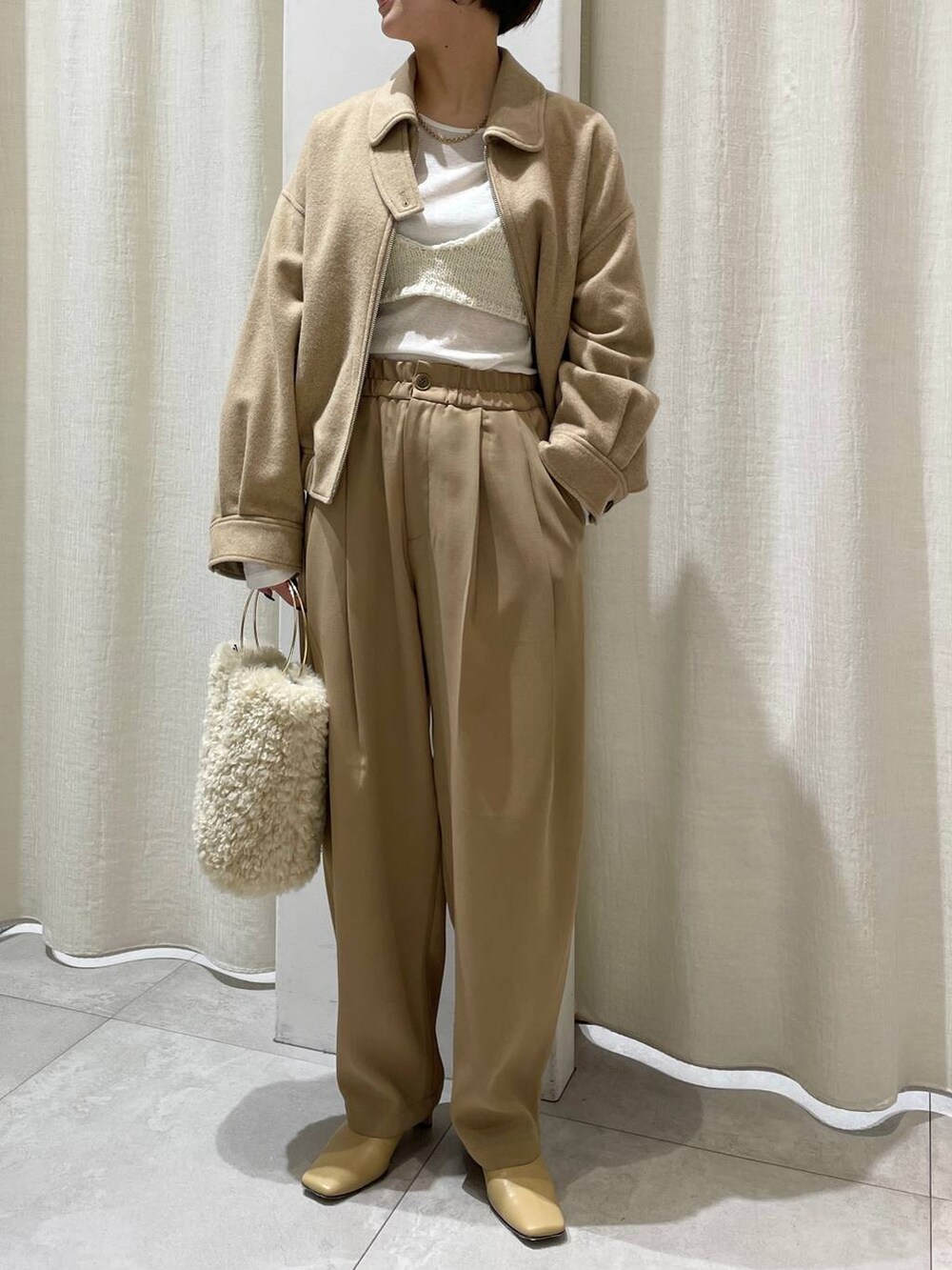 ホワイト系のハンドバッグ、ホワイト系のニット/セーター、ベージュ系のブルゾンを着用したレディースの秋コーディネートの5枚目の写真