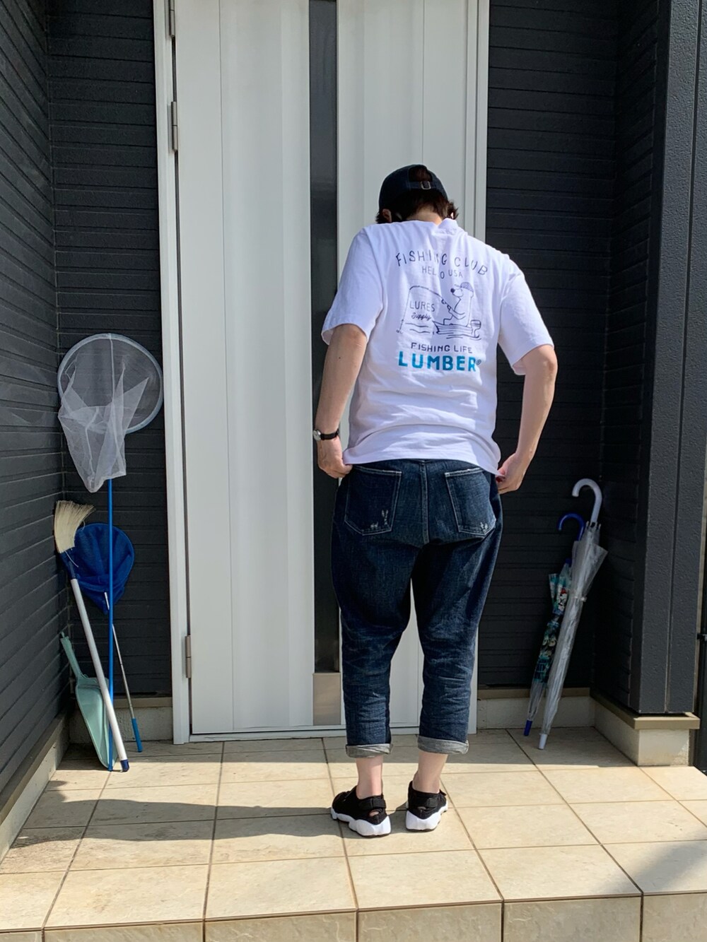 ブルー系のデニムパンツ、ブラック系のサンダル、ホワイト系のTシャツ/カットソーを着用したレディースの夏コーディネートの2枚目の写真