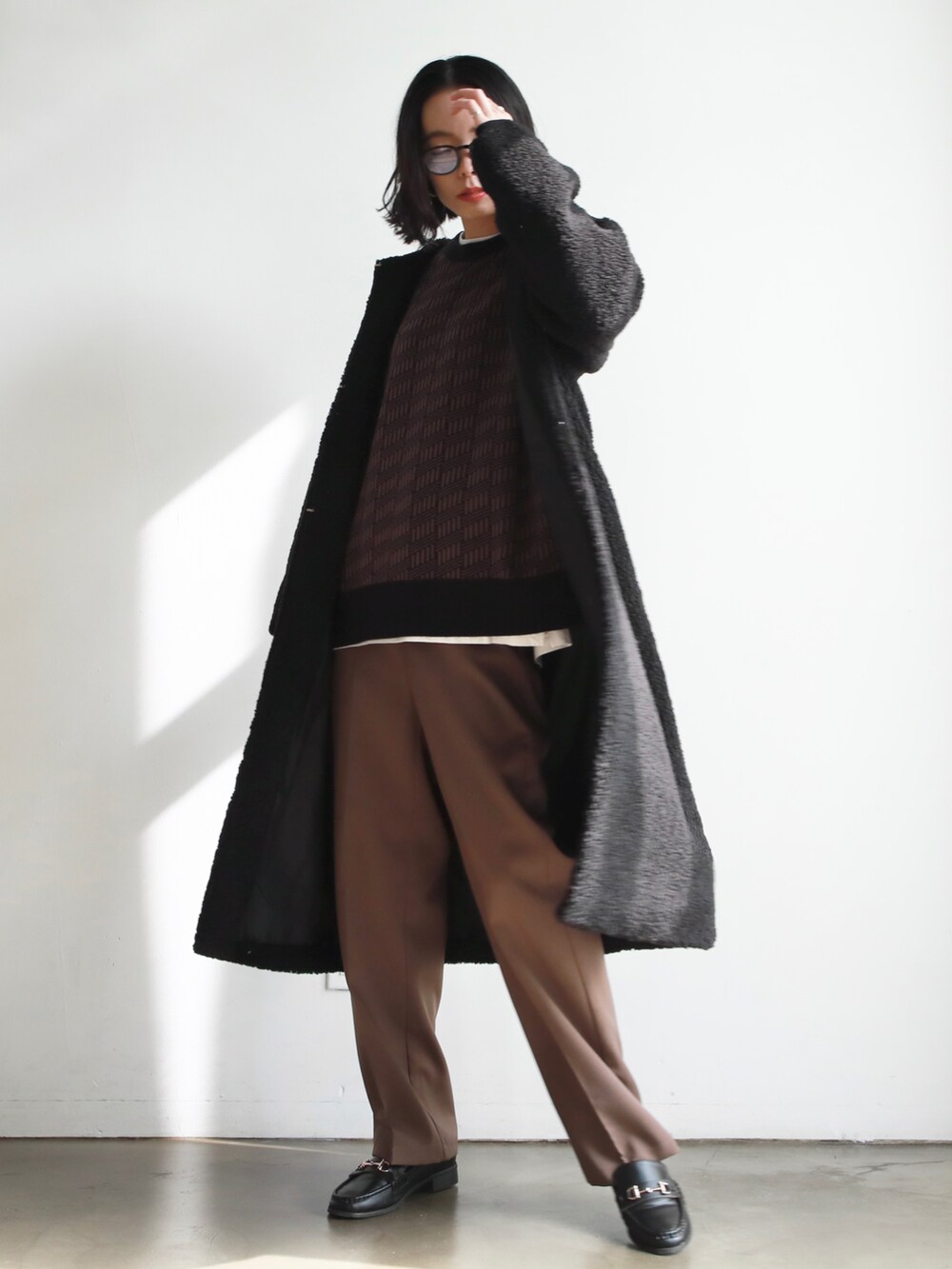 ブラック系のノーカラーコート、ブラック系のハンドバッグ、ブルー系のニット/セーターを着用したレディースの冬コーディネートの2枚目の写真