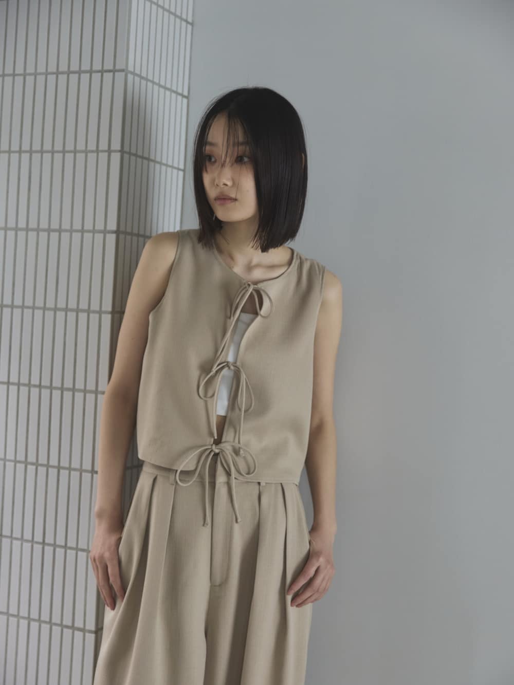 ホワイト系のスラックス、ホワイト系のベスト、ブラウン系のトートバッグを着用したレディースの夏コーディネートの3枚目の写真