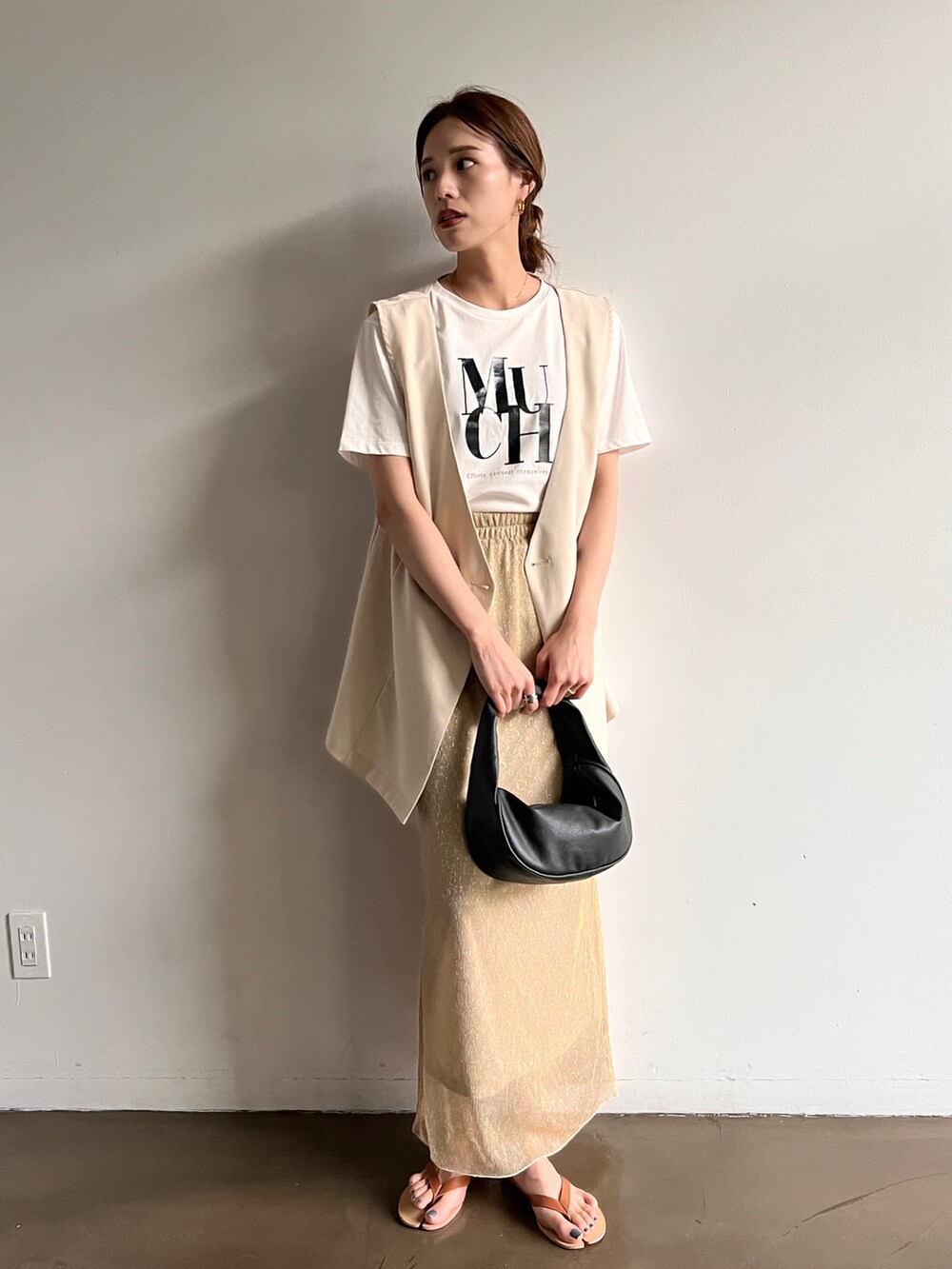 ブラック系のハンドバッグ、ベージュ系のスカート、ホワイト系のベストを着用したレディースの夏コーディネートの2枚目の写真