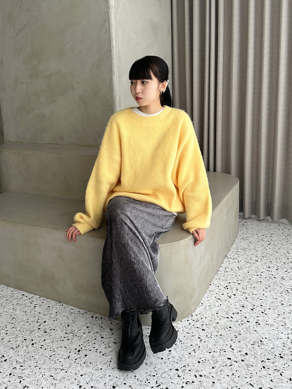 イエロー系のニット/セーター、グレー系のスカート、ブラック系のブーツを着用したレディースの冬コーディネートの4枚目の写真