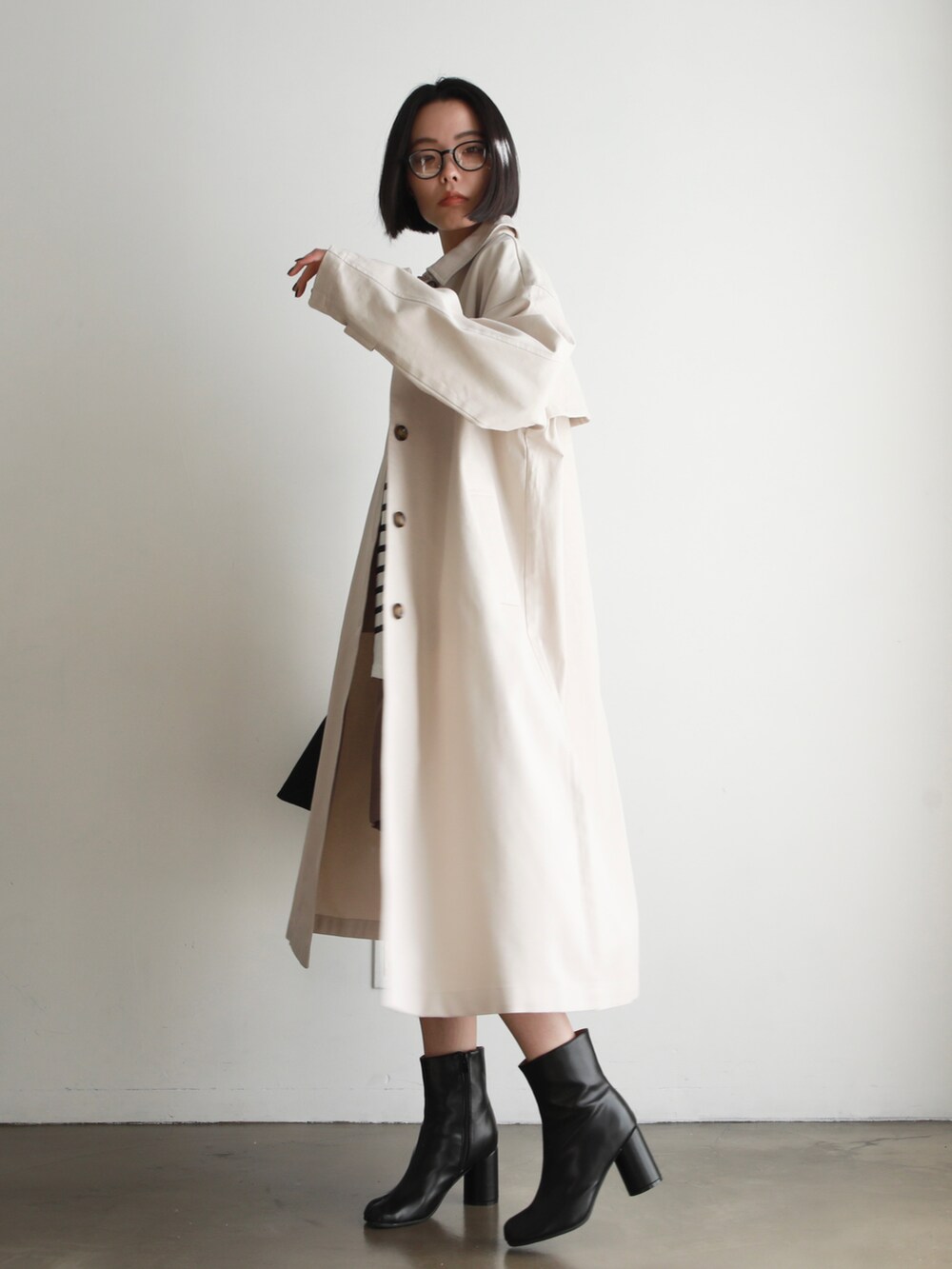 ホワイト系のステンカラーコート、ホワイト系のTシャツ/カットソー、ブラック系のハンドバッグを着用したレディースの冬コーディネートの2枚目の写真