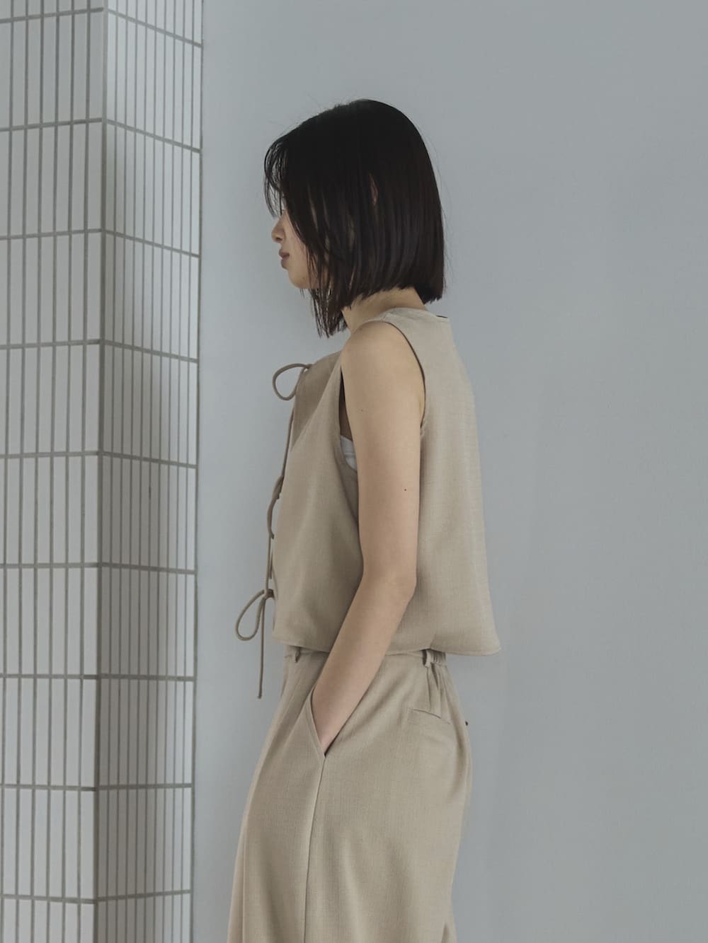 ホワイト系のスラックス、ホワイト系のベスト、ブラウン系のトートバッグを着用したレディースの夏コーディネートの4枚目の写真