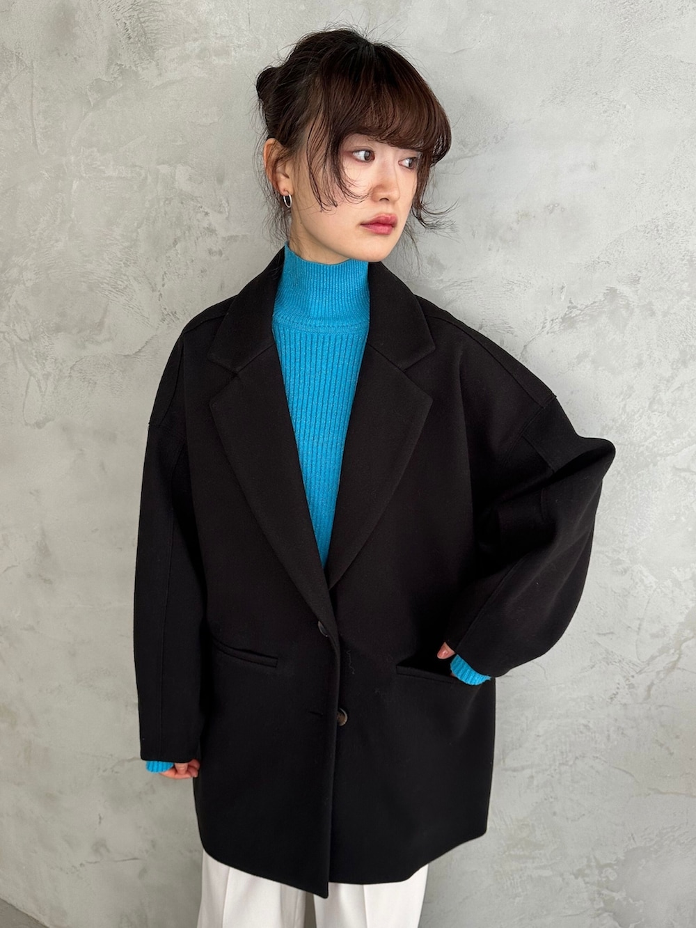 ブラック系のチェスターコート、ブルー系のニット/セーター、シルバー系のショルダーバッグを着用したレディースの冬コーディネートの3枚目の写真