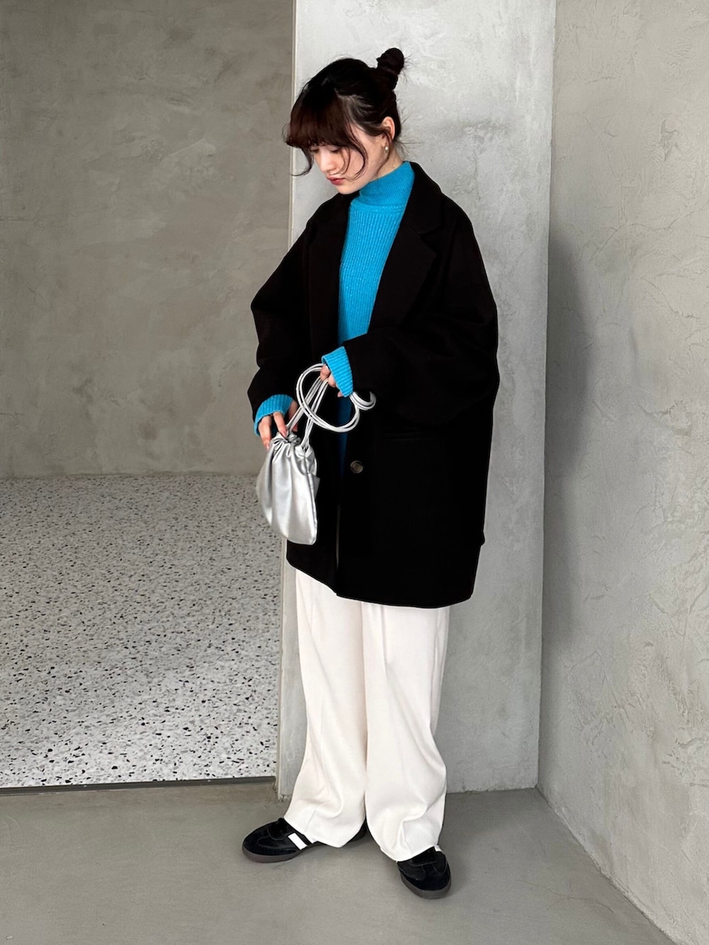 ブラック系のチェスターコート、ブルー系のニット/セーター、シルバー系のショルダーバッグを着用したレディースの冬コーディネートの2枚目の写真