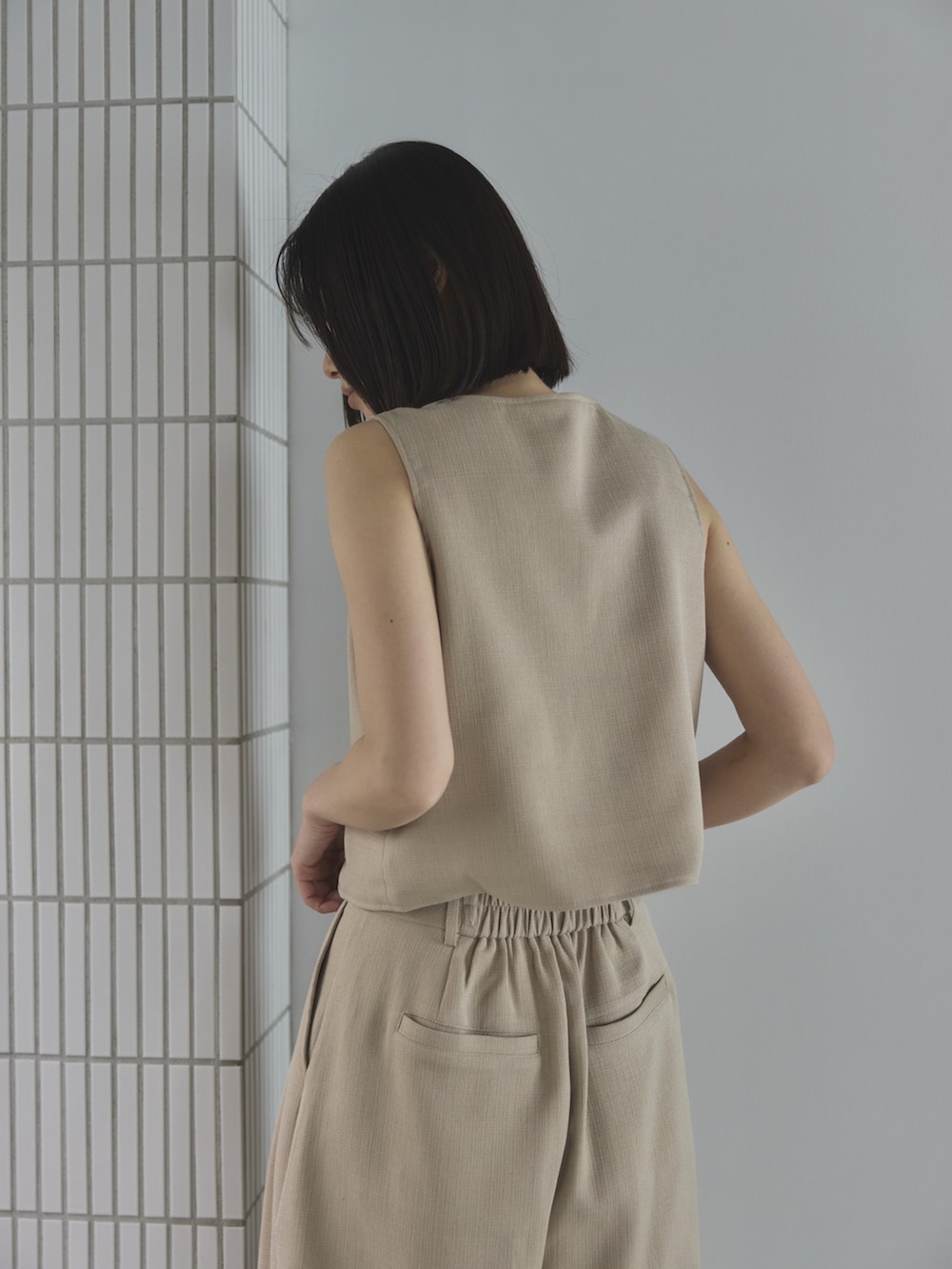 ホワイト系のスラックス、ホワイト系のベスト、ブラウン系のトートバッグを着用したレディースの夏コーディネートの5枚目の写真