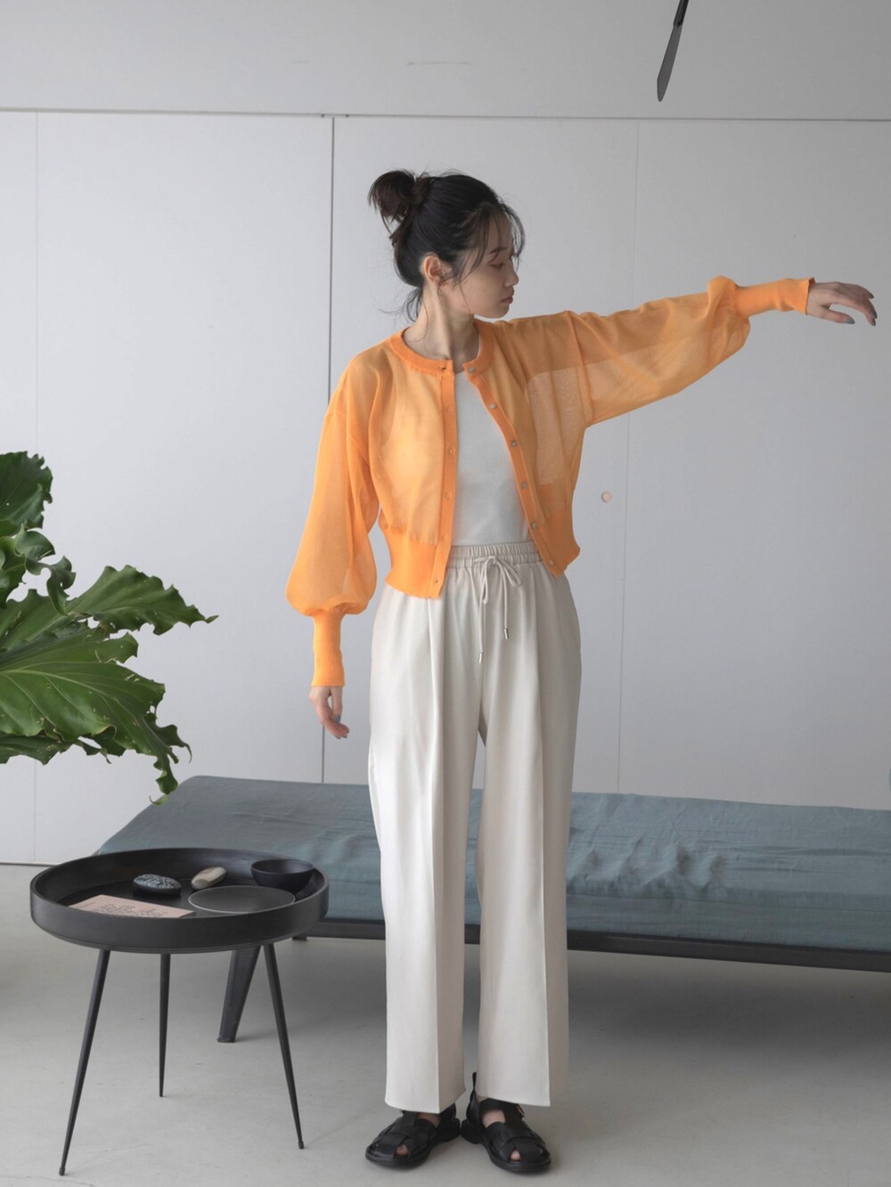 ホワイト系のスラックス、オレンジ系のカーディガン/ボレロ、ホワイト系のタンクトップを着用したレディースの春コーディネートの2枚目の写真