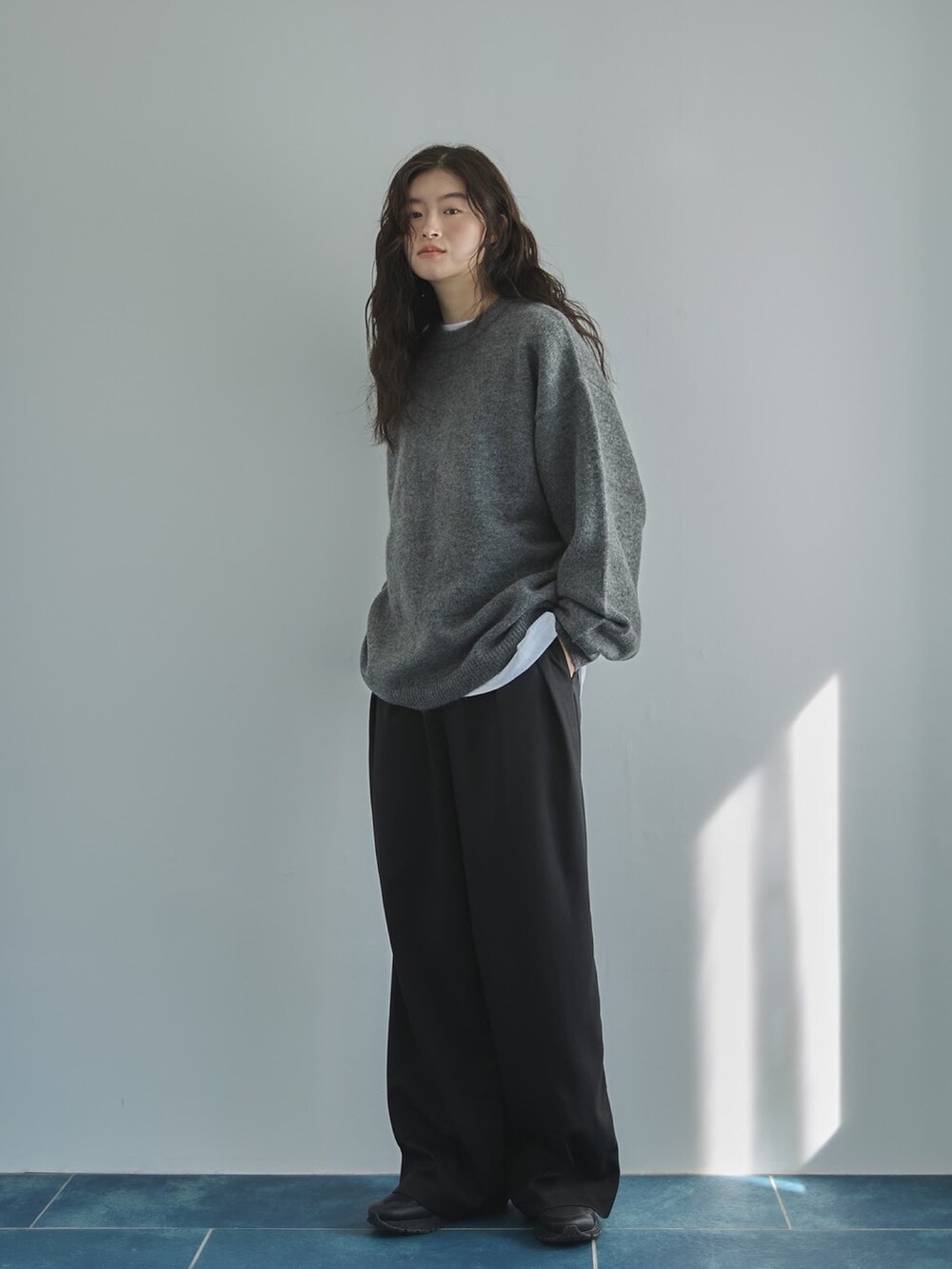 グレー系のニット/セーター、ホワイト系のTシャツ/カットソー、ブラック系のスラックスを着用したレディースの秋コーディネートの2枚目の写真