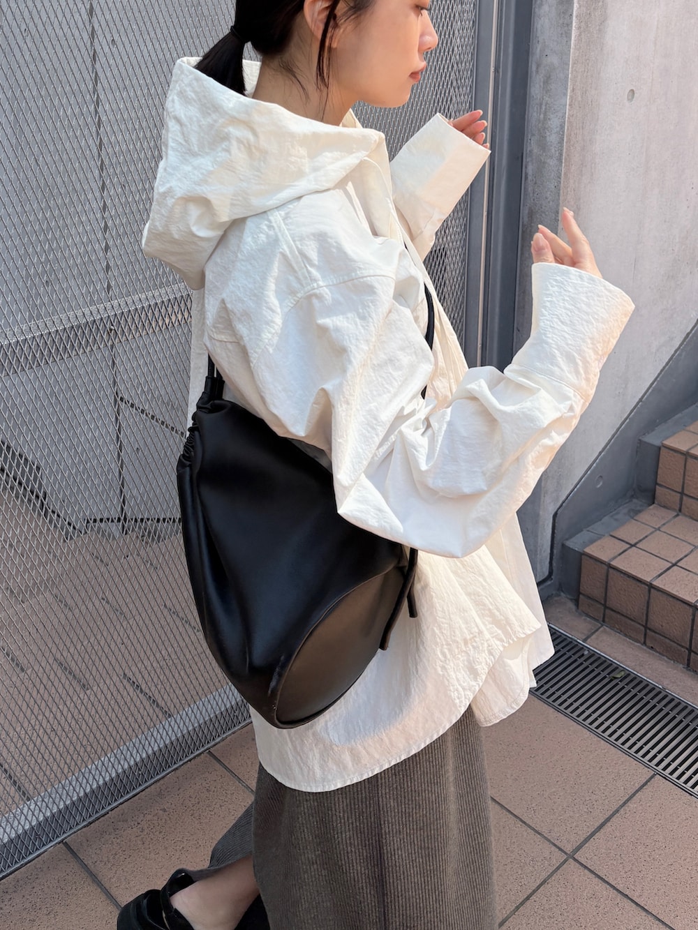 ブラック系のショルダーバッグ、ホワイト系のシャツ/ブラウス、グレー系のスカートを着用したレディースの春コーディネートの2枚目の写真