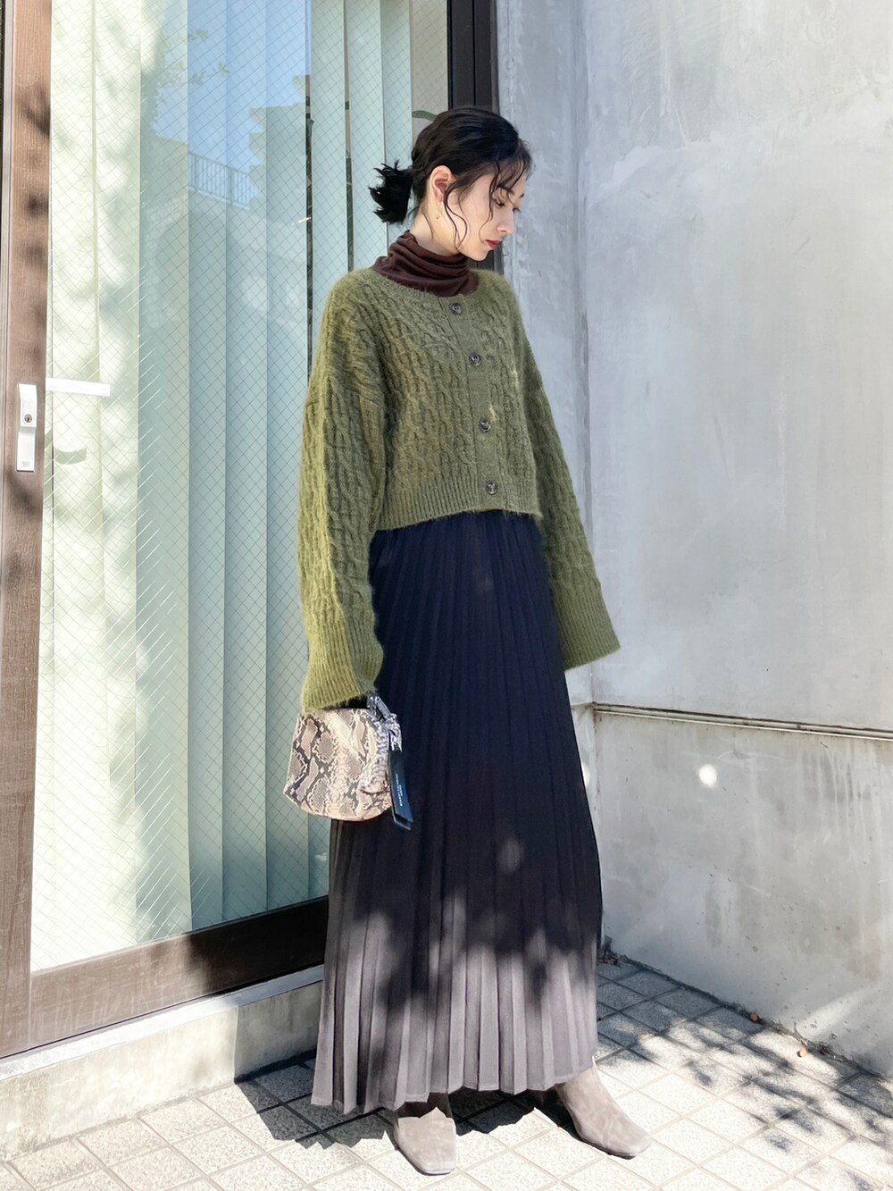 グリーン系のカーディガン/ボレロ、ブラック系のスカート、グレー系のブーツを着用したレディースの秋コーディネートの2枚目の写真