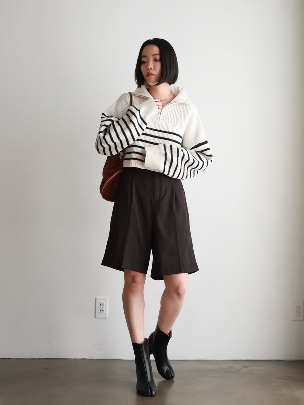 ブラック系のハンドバッグ、ブラウン系のスラックス、ホワイト系のニット/セーターを着用したレディースの春コーディネートの2枚目の写真