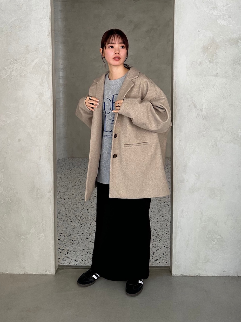 ブラック系のチェスターコート、グレー系のスウェット、ブラック系のスカートを着用したレディースの冬コーディネートの2枚目の写真