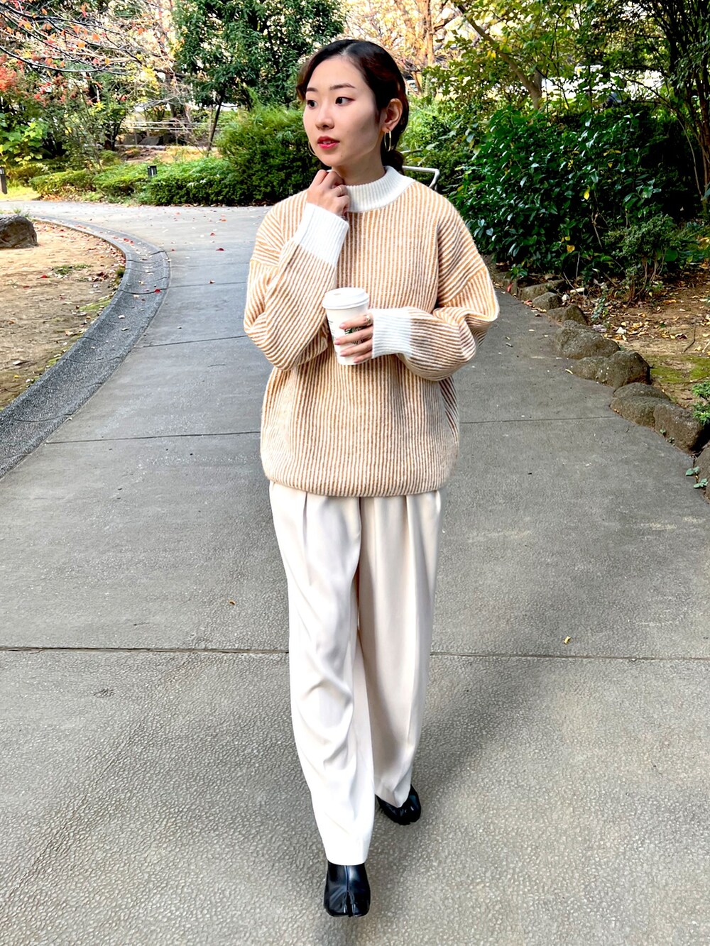 オレンジ系のニット/セーター、ホワイト系のスラックス、ブラック系のブーツを着用したレディースの秋コーディネートの2枚目の写真