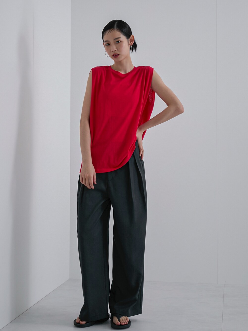 レッド系のタンクトップ、グレー系のスラックス、ブラック系のサンダルを着用したレディースの春コーディネートの2枚目の写真