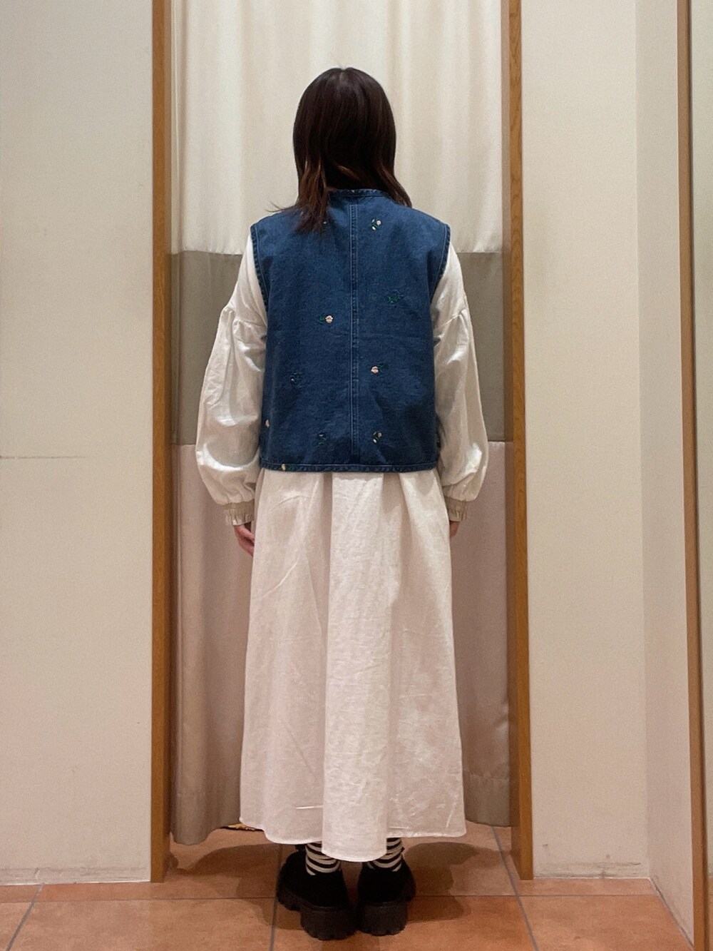 ブルー系のベスト、ホワイト系のワンピース、ブラック系のモカシン/デッキシューズを着用したレディースの冬コーディネートの2枚目の写真