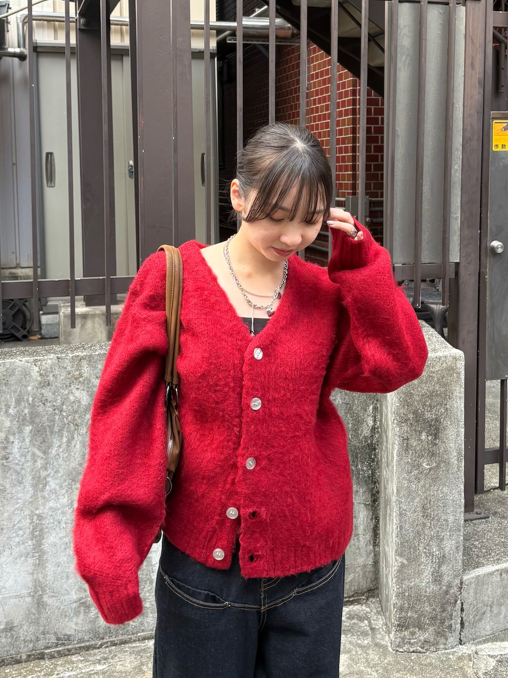 レッド系のカーディガン/ボレロ、ブルー系のデニムパンツ、ブラウン系のショルダーバッグを着用したレディースの秋コーディネートの2枚目の写真