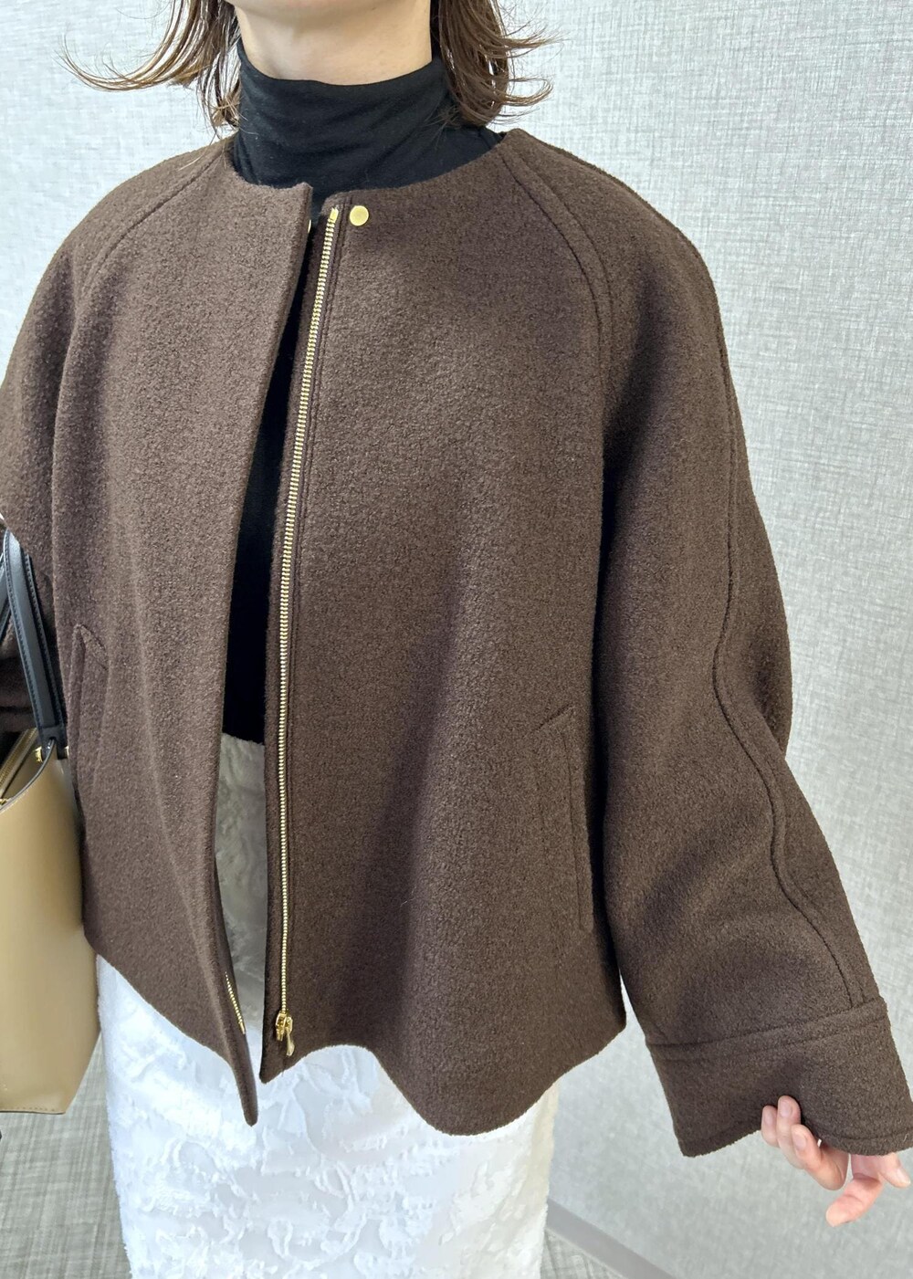 ベージュ系のトートバッグ、ブラック系のブーツ、ホワイト系のスカートを着用したレディースの秋コーディネートの5枚目の写真