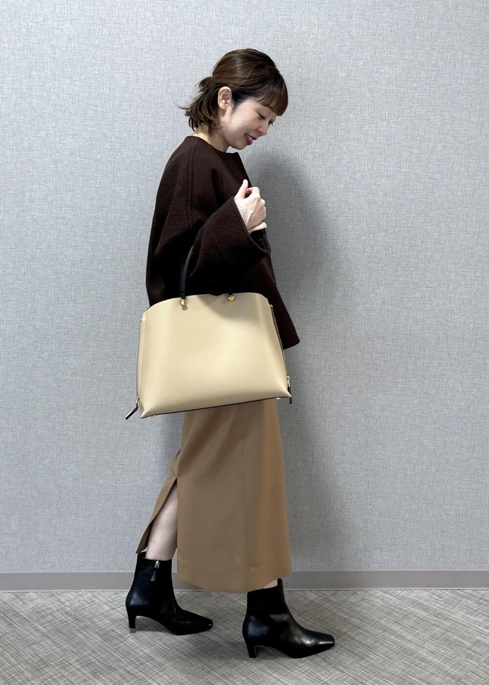 ベージュ系のトートバッグ、ブラック系のブーツ、ベージュ系のスカートを着用したレディースの秋コーディネートの2枚目の写真
