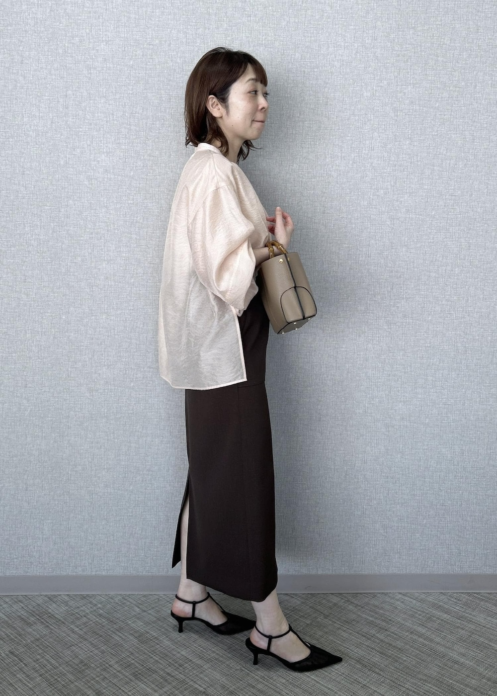 ブラック系のパンプス、ベージュ系のハンドバッグ、ブラウン系のスカートを着用したレディースの冬コーディネートの2枚目の写真