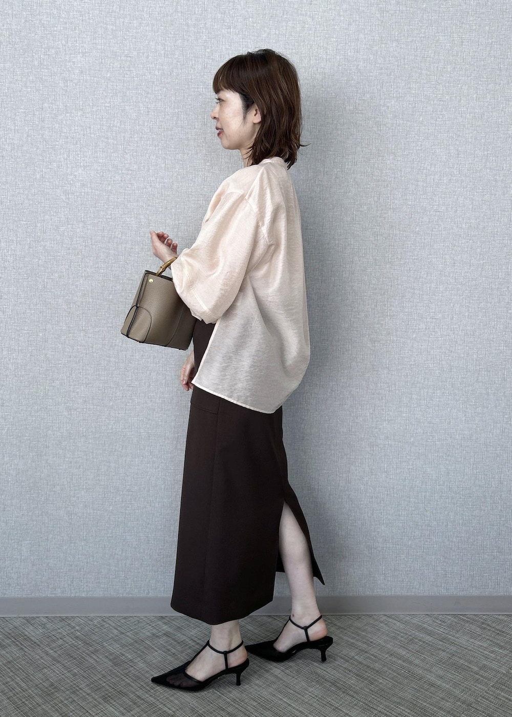 ブラック系のパンプス、ベージュ系のハンドバッグ、ブラウン系のスカートを着用したレディースの冬コーディネートの3枚目の写真