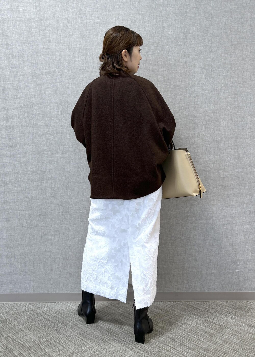 ベージュ系のトートバッグ、ブラック系のブーツ、ホワイト系のスカートを着用したレディースの秋コーディネートの4枚目の写真