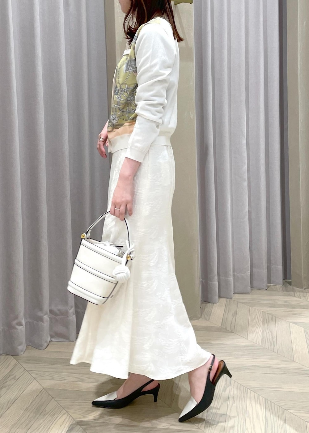 ホワイト系のハンドバッグ、ホワイト系のカーディガン/ボレロ、ブラック系のパンプスを着用したレディースの春コーディネートの2枚目の写真