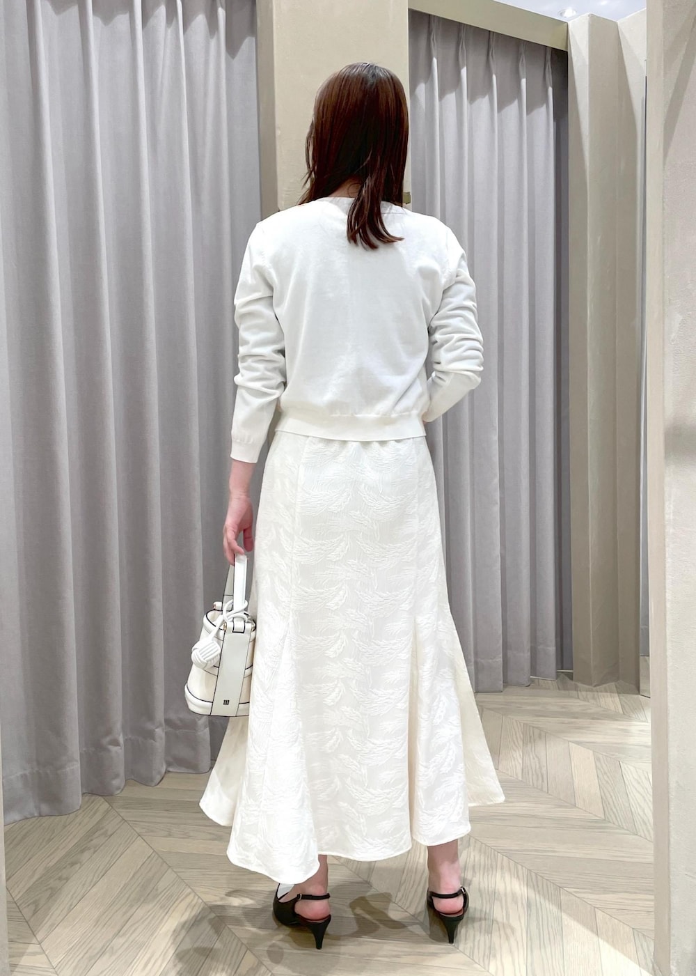 ホワイト系のハンドバッグ、ホワイト系のカーディガン/ボレロ、ブラック系のパンプスを着用したレディースの春コーディネートの3枚目の写真